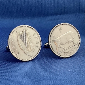 May include: Silver cufflinks featuring coin designs. One cufflink displays a harp and the year 1966, while the other shows a bull and the inscription "1 shilling". The cufflinks are set against a blue background.