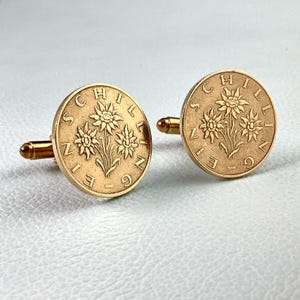 Può includere: Un paio di gemelli dorati. Ogni gemello presenta un design circolare con un motivo floreale e la scritta "SCHILL ZIEG". I gemelli hanno un design classico ed elegante.