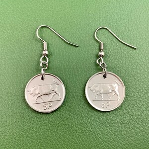 May include: Silver-toned dangle earrings featuring a coin design. Each earring showcases a bull image and the number "5P". The earrings have a simple hook closure and are displayed against a green background.