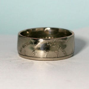 May include: Silver ring made from a 1977 US coin. The ring features the words "In God We Trust" and the year "1977" engraved on the band.