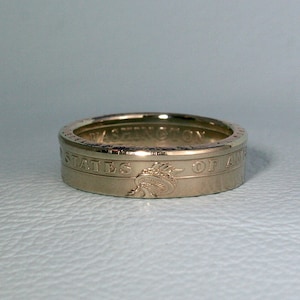 Op de afbeelding: Een gouden ring gemaakt van een Amerikaanse kwart dollar. De ring heeft de inscriptie "STATES OF AMERICA" en een afbeelding van Lady Liberty.