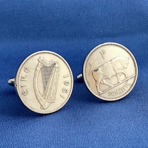 May include: Silver cufflinks featuring Irish coins. One cufflink displays a harp and the year 1951, while the other shows a bull and the word "scilling". The cufflinks are set against a blue background.