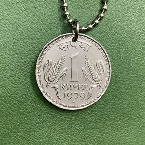 May include: A silver pendant necklace featuring a 1979 Indian 1 Rupee coin. The coin has a design of two wheat stalks and the text "1 Rupee 1979".