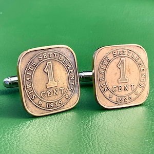 May include: A pair of bronze cufflinks. Each square cufflink features a coin design with the text "STRAITS SETTLEMENTS" and "1 CENT", with the years 1919 and 1920. The cufflinks have a silver-tone bar.