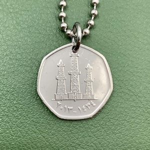 May include: A silver necklace with a silver pendant featuring three oil derricks and the text "١٩٧٦ - ١٩٨١ - ١٩٨٦".