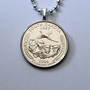 May include: Silver necklace with a South Dakota quarter coin pendant featuring the Mount Rushmore National Memorial and a pheasant. The coin reads "South Dakota 1889" and "E Pluribus Unum" with the year "2006" below the memorial.