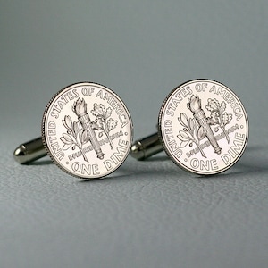 May include: A pair of silver cufflinks featuring the obverse side of a United States dime coin. Each cufflink features the inscription "UNITED STATES OF AMERICA" and "ONE DIME" along with the inscription "E PLURIBUS UNUM".
