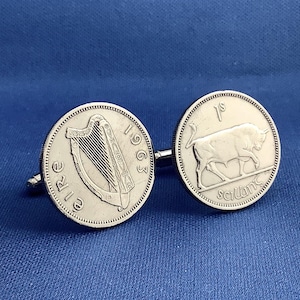 May include: Silver cufflinks featuring Irish coins. One cufflink displays a harp and the year 1963, while the other shows a bull and the inscription "1s". The cufflinks are set against a blue background.