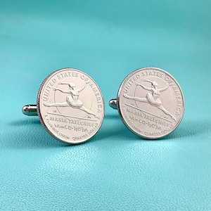 May include: Silver cufflinks featuring a quarter coin design with the words "United States of America" and "Maria Tallchief" engraved. The coin design depicts a ballerina in mid-leap. The cufflinks have a silver finish.