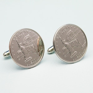 May include: A pair of silver cufflinks featuring the design of a US quarter coin with the Statue of Liberty and the text "NEW YORK 1788 GATEWAY TO FREEDOM 2001 E PLURIBUS UNUM".