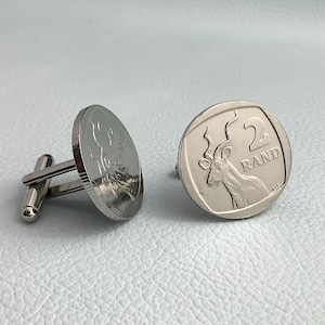 以下が含まれることがあります： スプリングボックの画像が刻まれた南アフリカの2ランド硬貨をあしらった、銀製のカフスボタンのペア。硬貨には「2ランド」の文字が刻まれています。