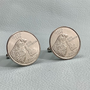 May include: A pair of silver cufflinks featuring the Idaho state quarter coin design. The coin features a  peregrine falcon, the state motto "Esto Perpetua", and the year 2007.