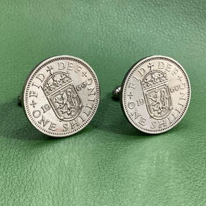 May include: A pair of silver cufflinks featuring a vintage British one shilling coin with the inscription "FID DEF 1966 ONE SHILLING".