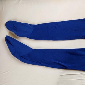 May include: A pair of royal blue fabric leg warmers, each with a foot covering and a flared top. The leg warmers are made of a soft, stretchy material and are laid out on a white surface.