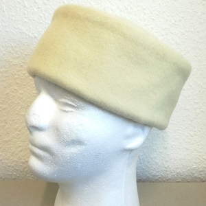 Op de afbeelding: Een crèmekleurig wollen hoofdband. Het hoofdband is breed en heeft een zachte, pluche textuur.