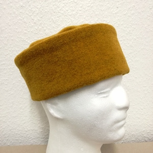 以下が含まれることがあります： 丸いクラウンと平らなつばを持つマスタードイエローのフェルトハット