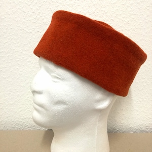 May include: A bright orange felt hat with a rounded top and a flat brim. The hat is on a white mannequin head.