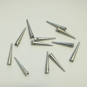 May include: A set of 10 silver metal cone-shaped spikes with a small hole at the top. The spikes are about 1 inch long.
