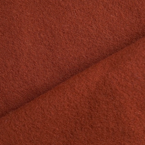 May include: Close-up of a rust-coloured fabric with a soft, fuzzy texture. The fabric is folded in half, showing the inside and outside of the material.