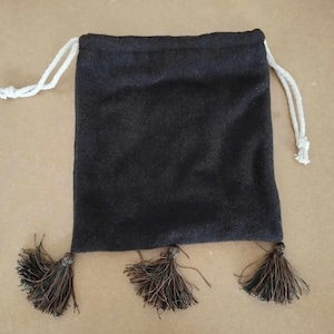 Peut inclure: Un sac à cordon noir avec trois pompons marrons. Le sac est fait d'un matériau doux et duveteux.