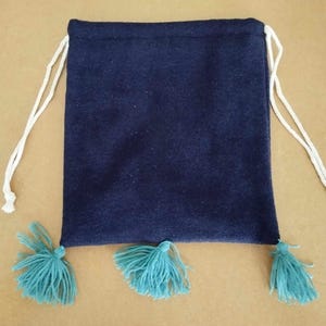 Peut inclure: Un sac à cordon bleu foncé avec trois pompons turquoise. Le sac est fait d'un tissu doux et duveteux.