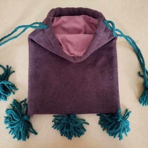 Peut inclure: Un sac à cordon de couleur pourpre avec des glands turquoise. Le sac est fait d'un tissu doux et duveteux.