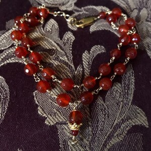 May include: A double-strand bracelet with red carnelian beads and gold accents. The bracelet has a clasp closure and a small carnelian pendant.