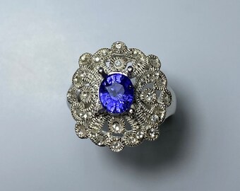 May include: A silver ring with a blue sapphire gemstone surrounded by smaller white gemstones in a delicate filigree design.