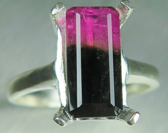 May include: A silver ring with a black and pink tourmaline gemstone. The gemstone is cut in a rectangular shape with a faceted design.