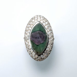 May include: A silver ring with a large green and purple gemstone surrounded by smaller clear gemstones.