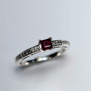 May include: A silver ring featuring a square ruby gemstone and a band of small diamonds.
