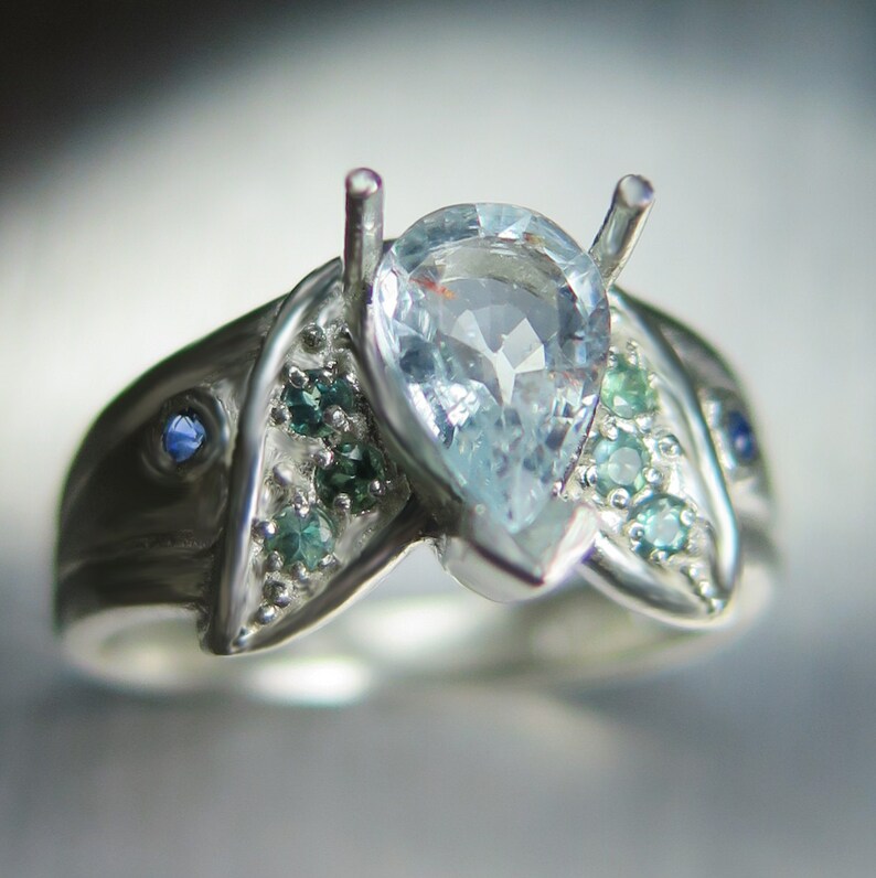 May include: A silver ring with a pear-shaped aquamarine gemstone surrounded by smaller green and blue gemstones.