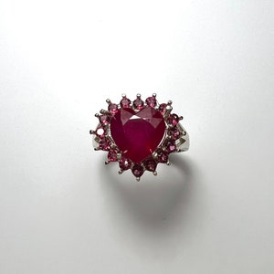 Puede incluir: Un anillo de plata con un gran rubí en forma de corazón rodeado de piedras de rubí más pequeñas.