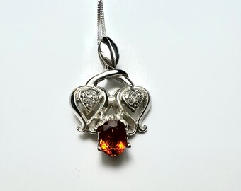 May include: A silver pendant necklace with a brown gemstone and two heart-shaped accents set with clear stones.