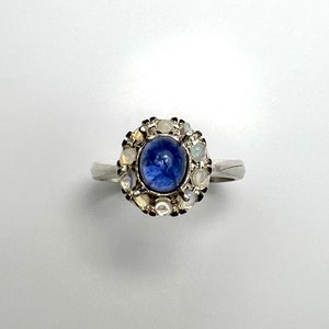 Puede incluir: Un anillo de plata con una piedra preciosa azul rodeada por un halo de piedras preciosas blancas más pequeñas.
