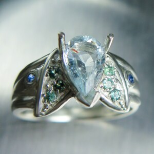 May include: A silver ring with a pear-shaped aquamarine gemstone surrounded by smaller blue and green gemstones.