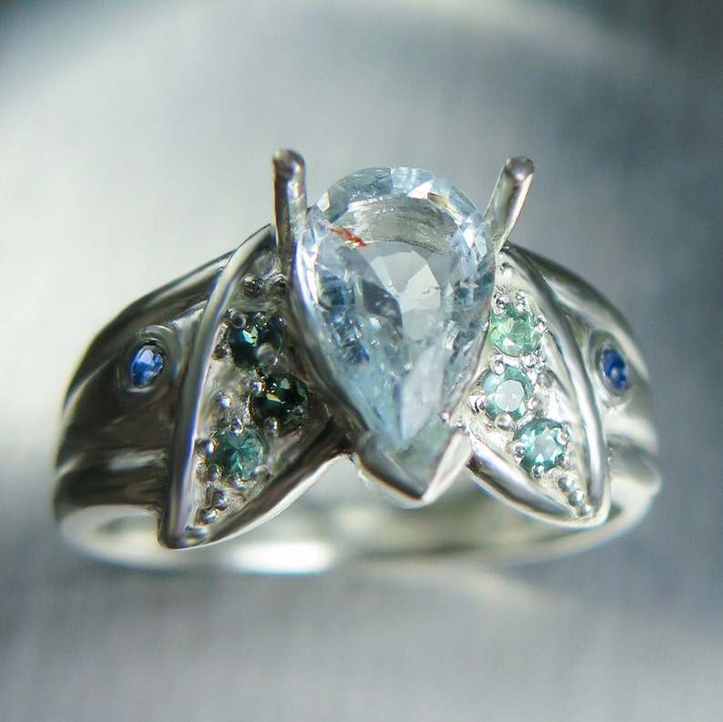 May include: A silver ring with a pear-shaped aquamarine gemstone surrounded by smaller blue and green gemstones.