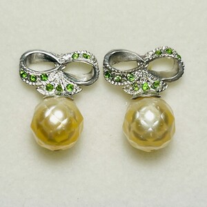 May include: A pair of silver earrings with a pearl drop and a green gemstone infinity symbol design.