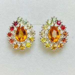 May include: A pair of silver earrings featuring a pear-shaped orange gemstone surrounded by smaller multi-coloured gemstones.