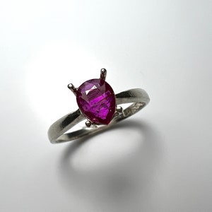May include: A pear-shaped, deep purple gemstone ring set in a silver band.