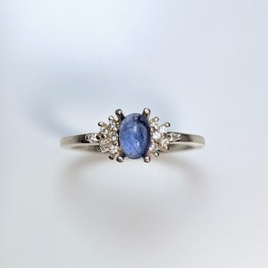 Puede incluir: Un anillo de plata con una piedra ovalada azul rodeada de piedras pequeñas transparentes.