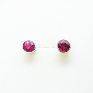 May include: A pair of silver stud earrings with small, round, red gemstones.