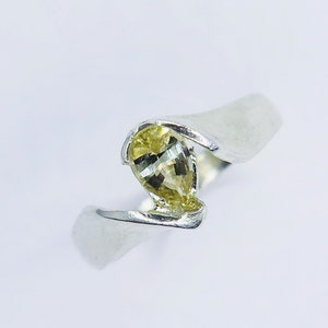 Puede incluir: Un anillo de plata con una piedra preciosa amarilla en forma de pera engastada en una banda retorcida.