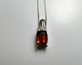 May include: A silver chain necklace with a pendant featuring a large, rectangular, brown gemstone surrounded by smaller, clear gemstones.