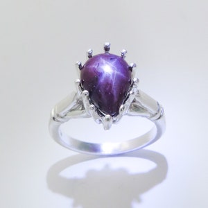 May include: A silver ring with a pear-shaped purple star sapphire gemstone set in a crown-like setting.