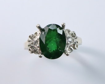 May include: A silver ring featuring a large, oval green gemstone set in a delicate, ornate design.