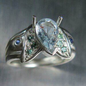 May include: A silver ring with a pear-shaped aquamarine gemstone surrounded by smaller green and blue gemstones.
