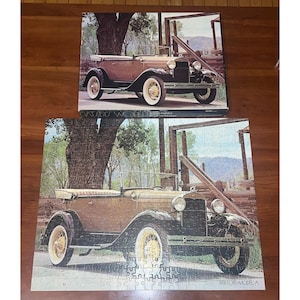 May include: Two vintage car puzzles. The top puzzle is complete, and the bottom puzzle is partially assembled. The puzzles feature a brown 1931 Ford Model A convertible with white-walled tires. The background includes a tree, wooden fence, and mountains.