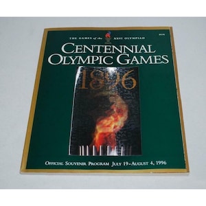 Puede incluir: Una portada de programa verde y dorada para los Juegos Olímpicos Centenarios de 1996 en Atlanta, Georgia. La portada presenta una imagen estilizada de la antorcha olímpica y el texto "THE GAMES of the XXVI OLYMPIAD CENTENNIAL OLYMPIC GAMES 1896 OFFICIAL SOUVENIR PROGRAM JULY 19-AUGUST 4, 1996".