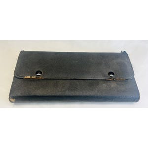 May include: A black, rectangular case with a flap closure secured by two snap closures. The case appears to be made of a textured material, possibly leather or a leather-like substance. The edges show signs of wear.